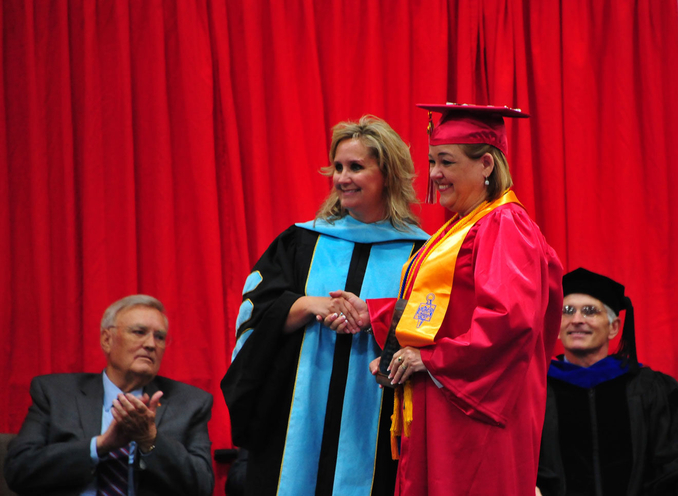 professor and graduate on stage in regalia