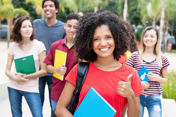 Attractive college-aged African-American girl holding a notebook and giving a thumbs-up.