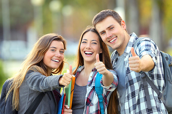 Two college-aged girls and one boy smiling and gesturing thumbs-up.