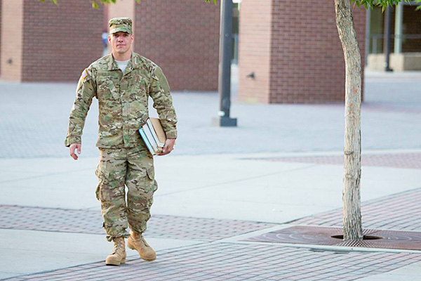 Young man in military fatigues walking on campus