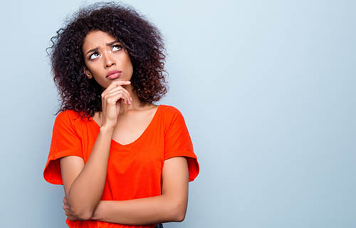 Portrait with copy space empty place of thoughtful minded woman with modern hairdo holding hand on chin looking up trying to find solution isolated on grey background