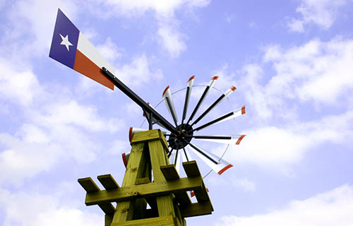 Wooden derick windmill with a Texas flag emblem against a beautiful blue sky.