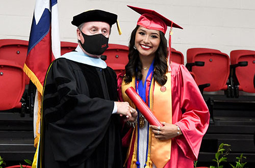 school leader shaking hand of smiling young lady in graduation regalia