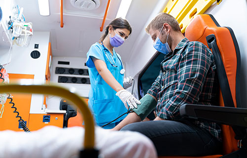 smiling young woman in medical smock treating patient in ambulance