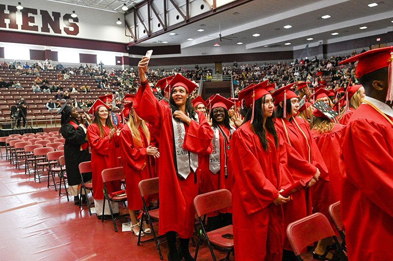 Students in a graduation ceremony smiling and standing in front of their seats