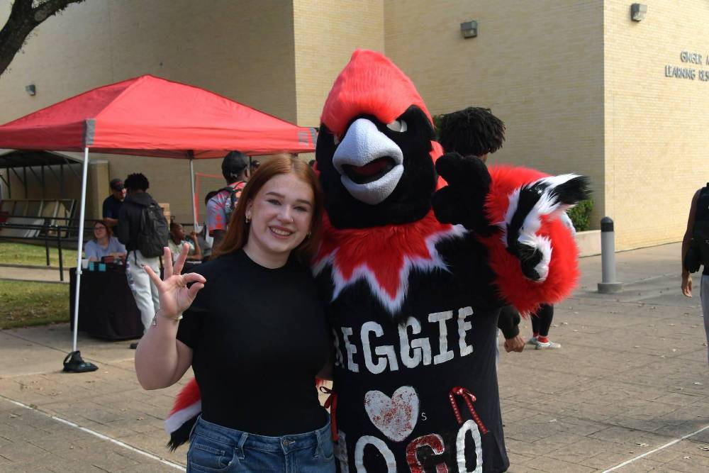 Baylie Sasser standing with Reggie holding up the cardinal salute
