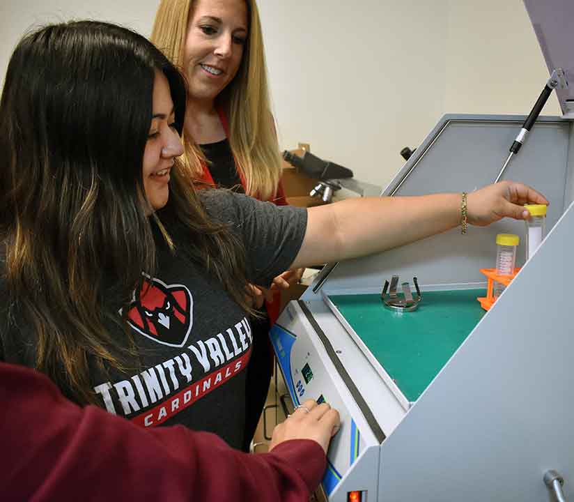Female student placing a test sample inside lab equipment machine