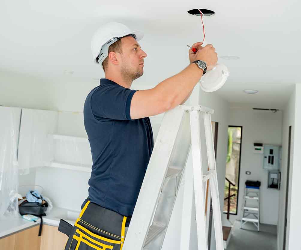 Electrician on ladder installing recessed lighting in the ceiling