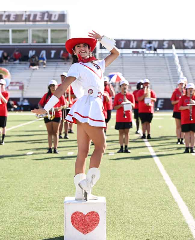Cardette posing on a box with the marching band on a football field
