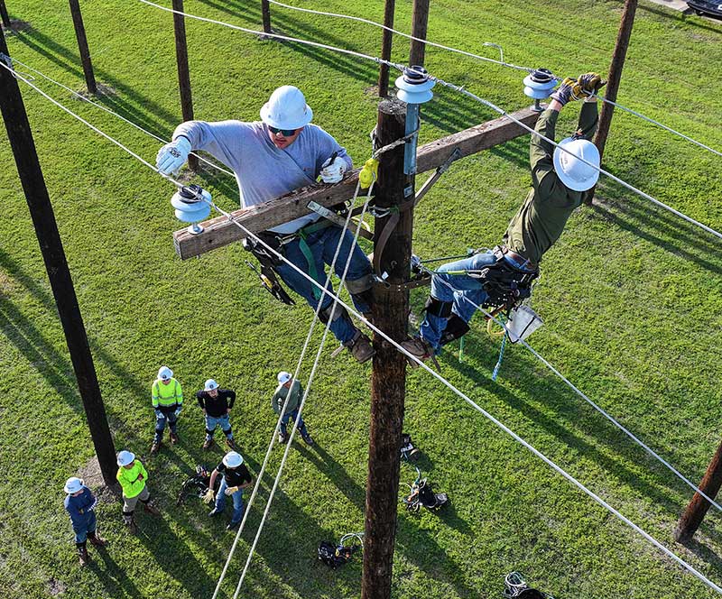 Electrical lineworkers stacked together on an utility pole waving to the camera