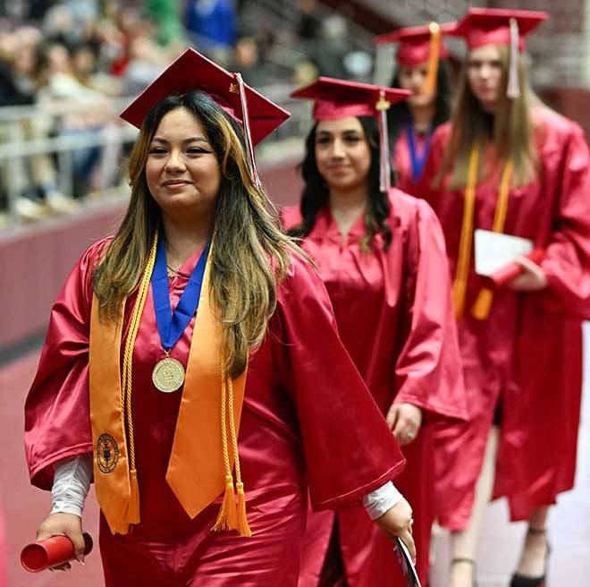 Students smiling and walking in a straight line to cross the stage.