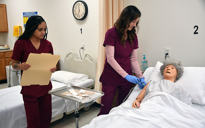 two medical nursing assistant students practicing with a manikin