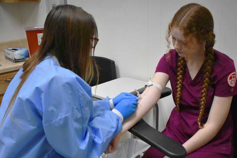female nurse drawing blood with a needle from another nurse
