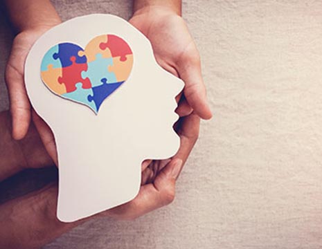 hands holding cardboard head cutout with heart-shaped brain