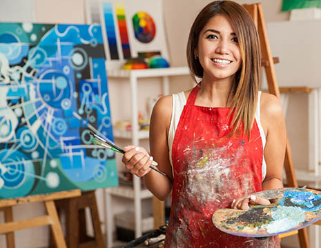smiling young lady in apron and holding paint brushes