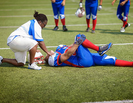 athletic trainer attending to injured football player holding his knee