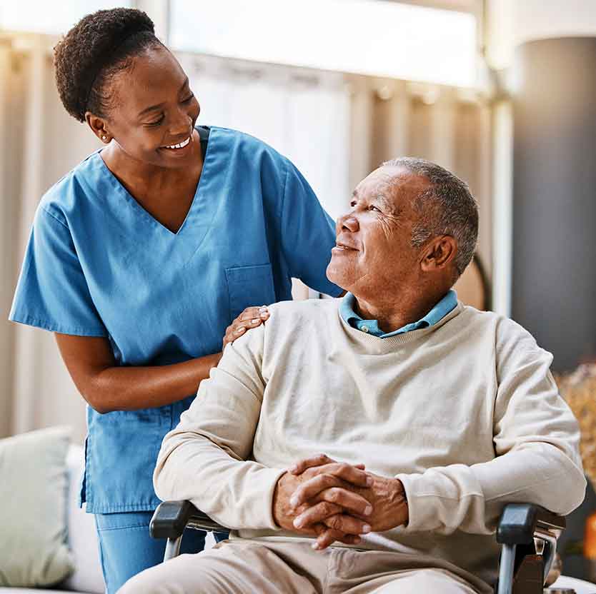 Female caretaker smiling at elderly man in wheel chair