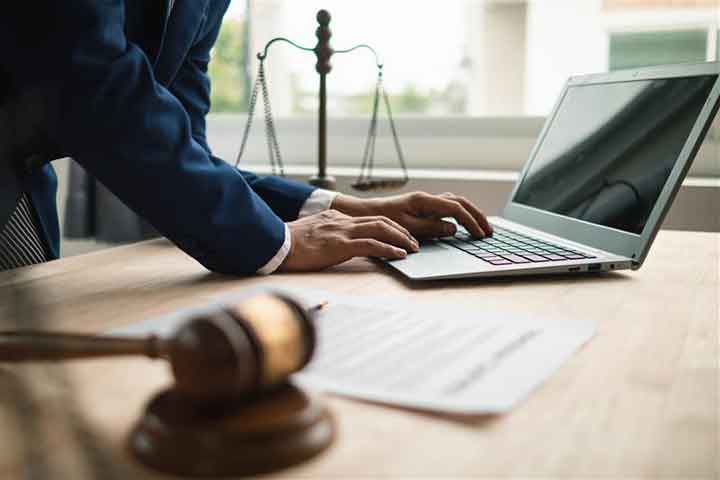 legal worker in front of a laptop on a desk with scales of justice and gavel