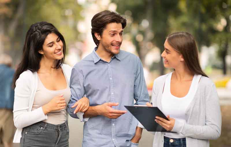 A couple walking down a city sidewalk and speaking with a sociologist
